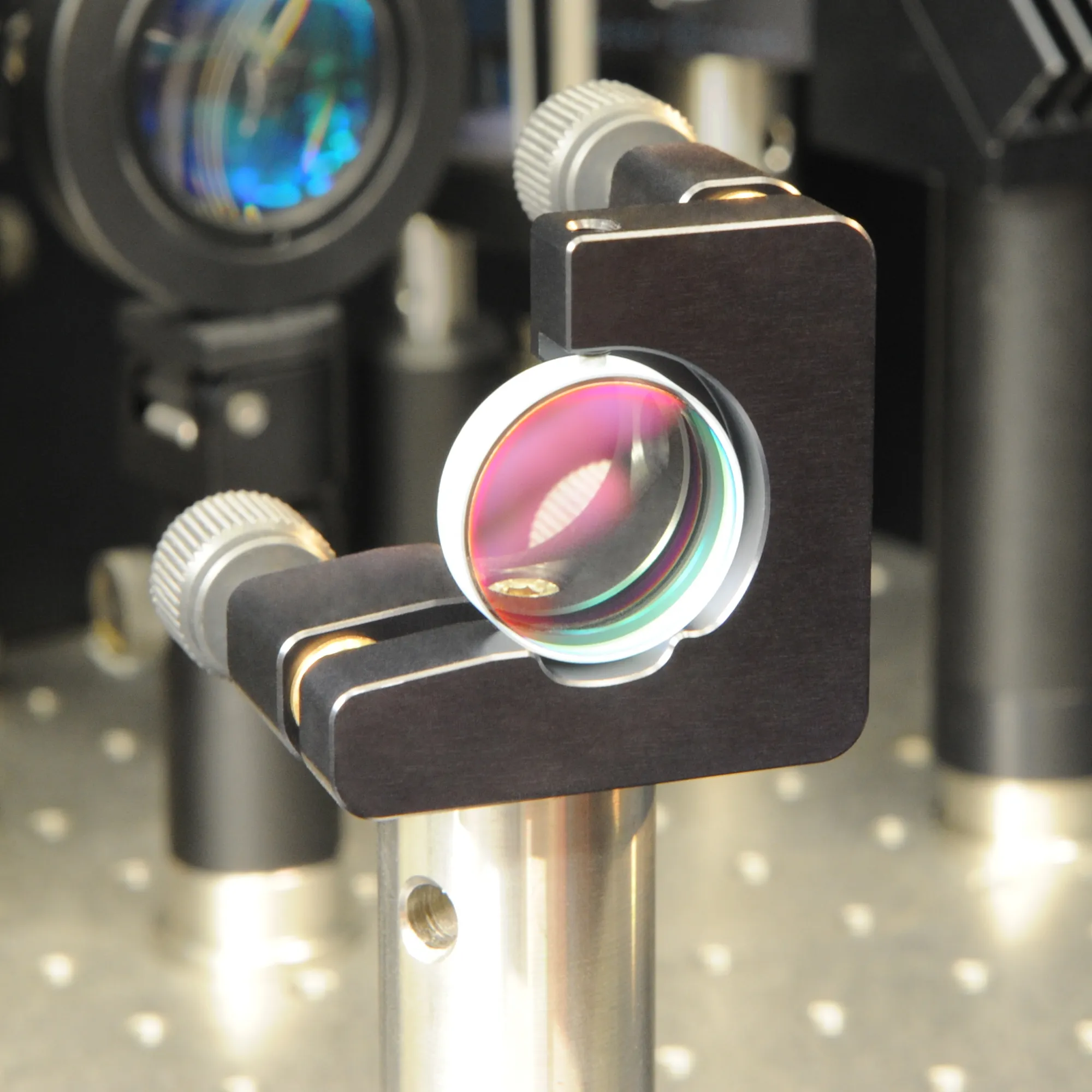 A pink and green dielectric mirror mounted in an optics laboratory